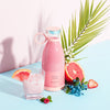 Pink juice bottle with a glass of juice, grapefruit, and strawberry on a light blue background